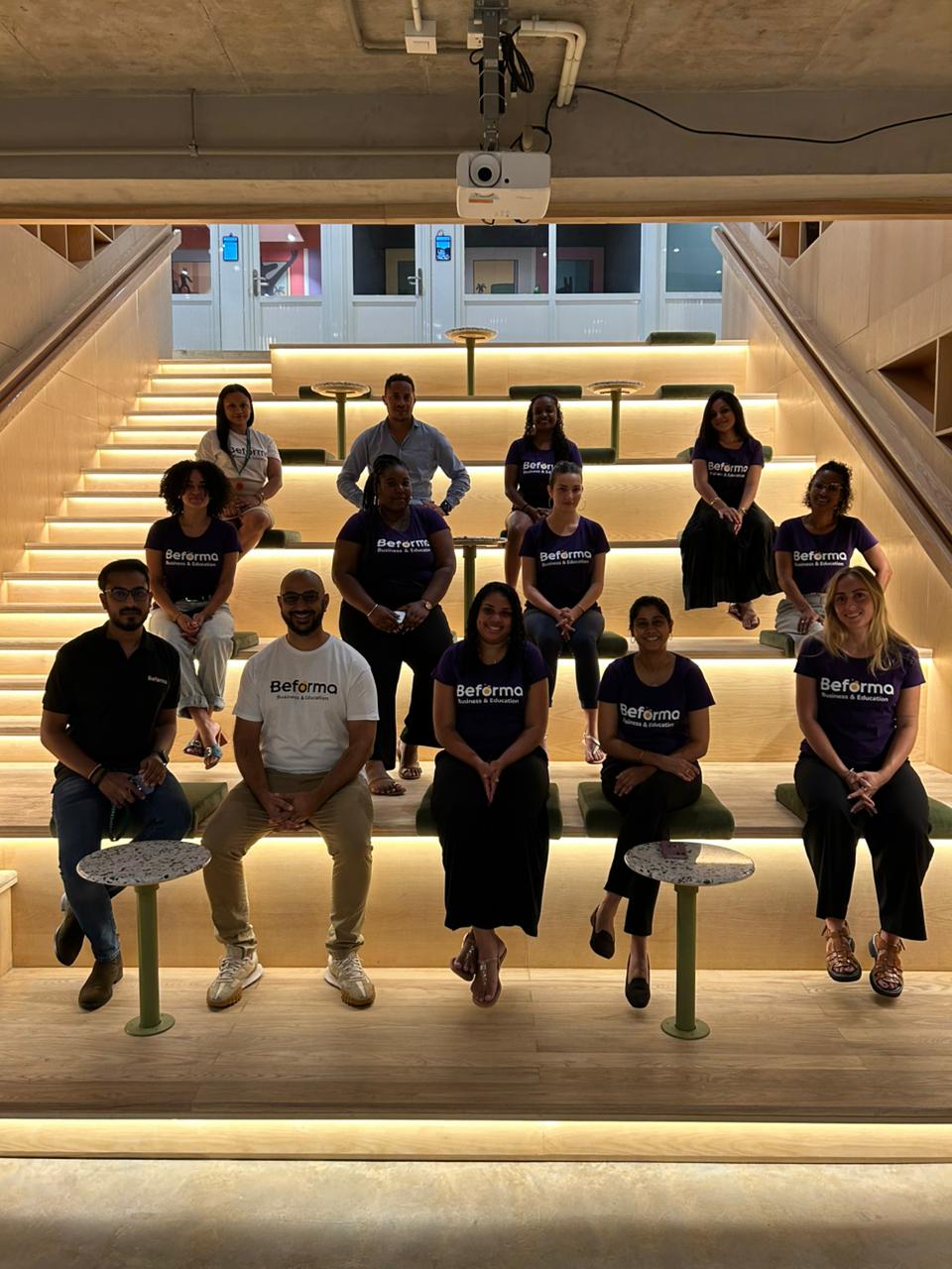 Photo de groupe de la promotion Bachelor RH Beforma sur un escalier en bois illuminé à l'Île Maurice — 15 personnes en t-shirts Beforma